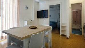 A small, modern room with a wooden dining table, white chairs, a television, and a shower area.