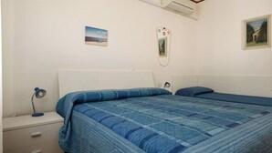 A bedroom with a bed, a nightstand, a lamp, and a wall-mounted air conditioner.