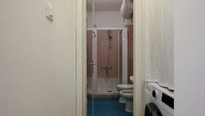 A bathroom with a shower, toilet, and washing machine.