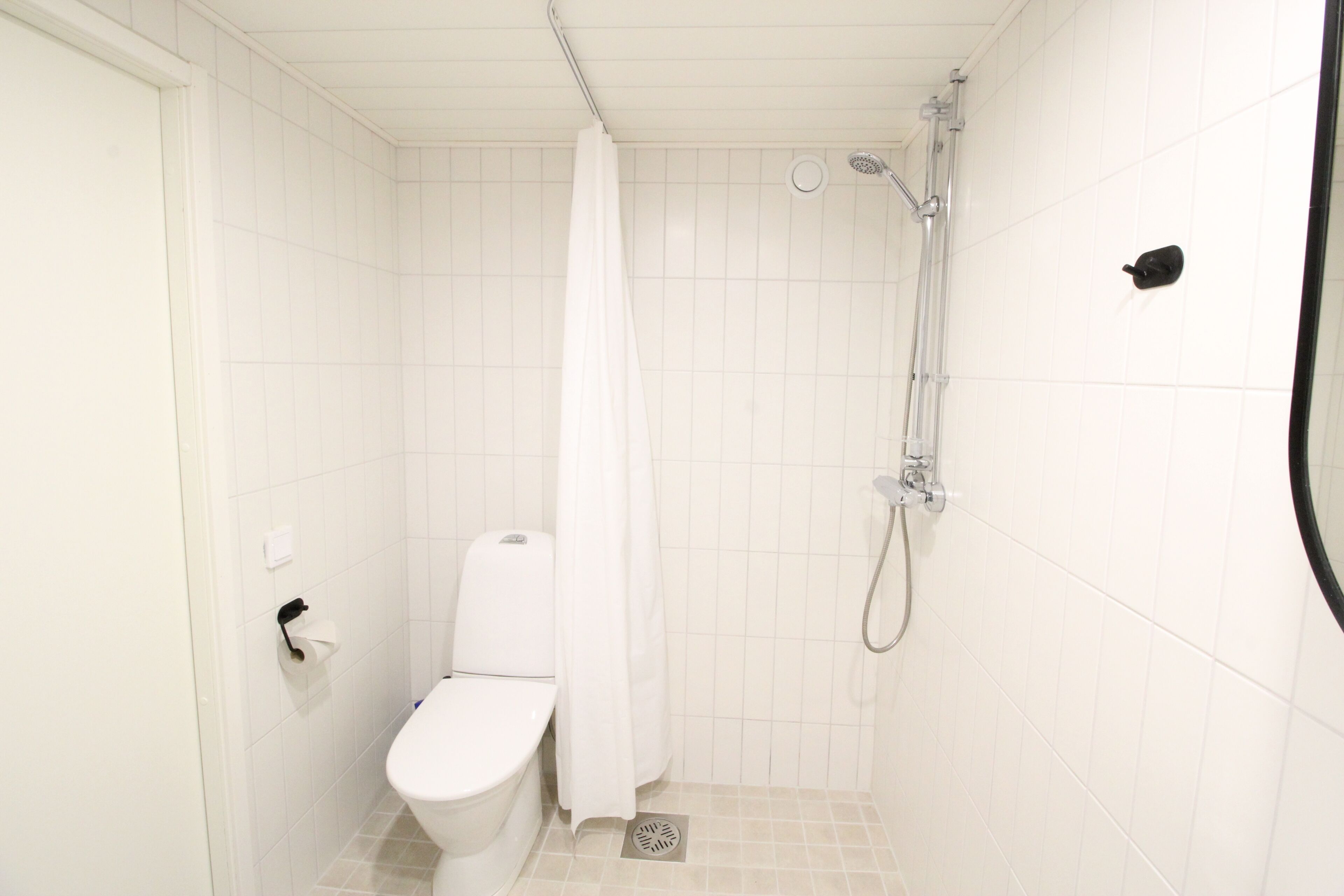 A small, white bathroom with a toilet, shower, and a white curtain.