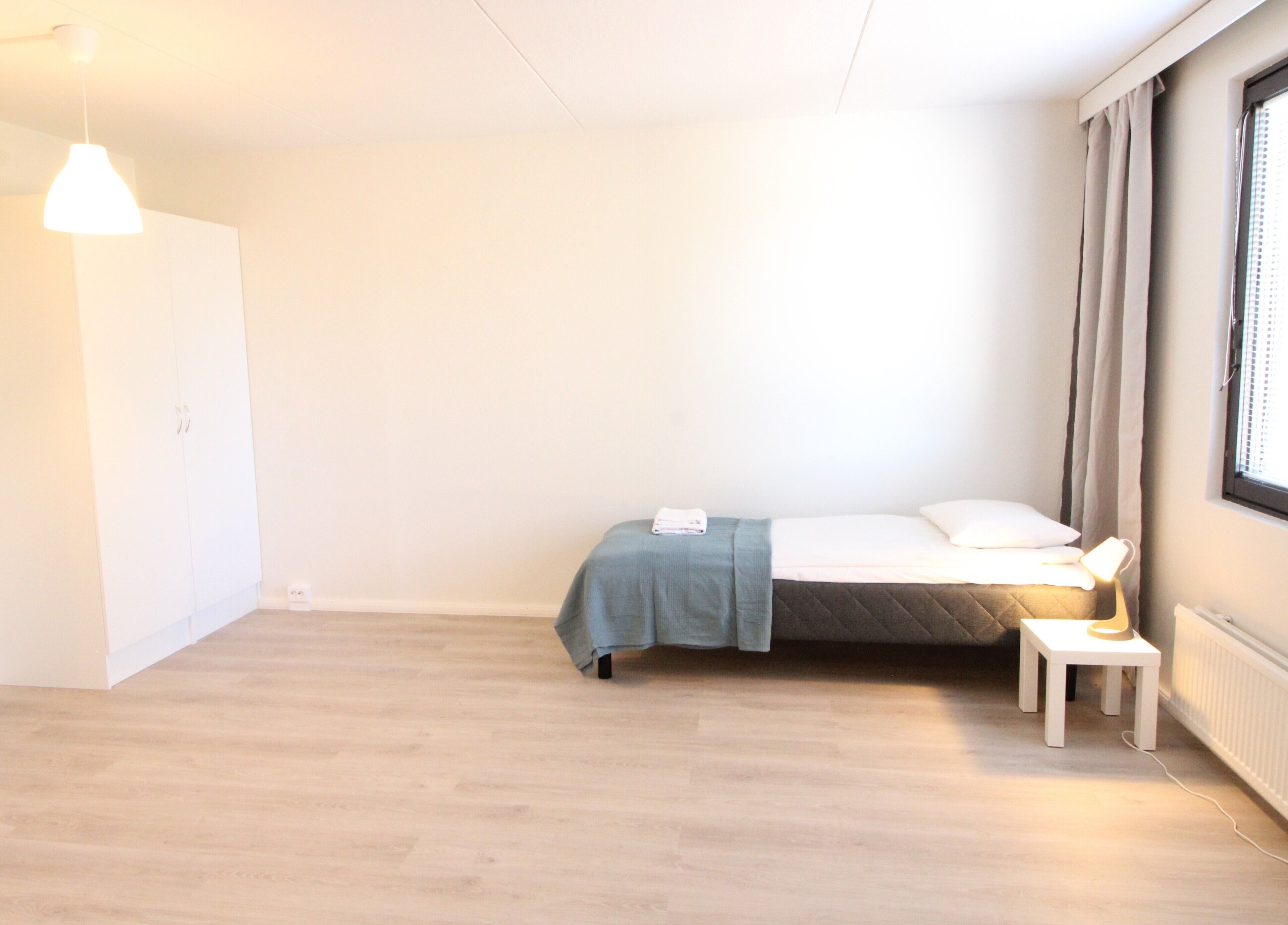 Ein schlichter Raum mit einem Bett, einem Nachttisch und einer Pendelleuchte.