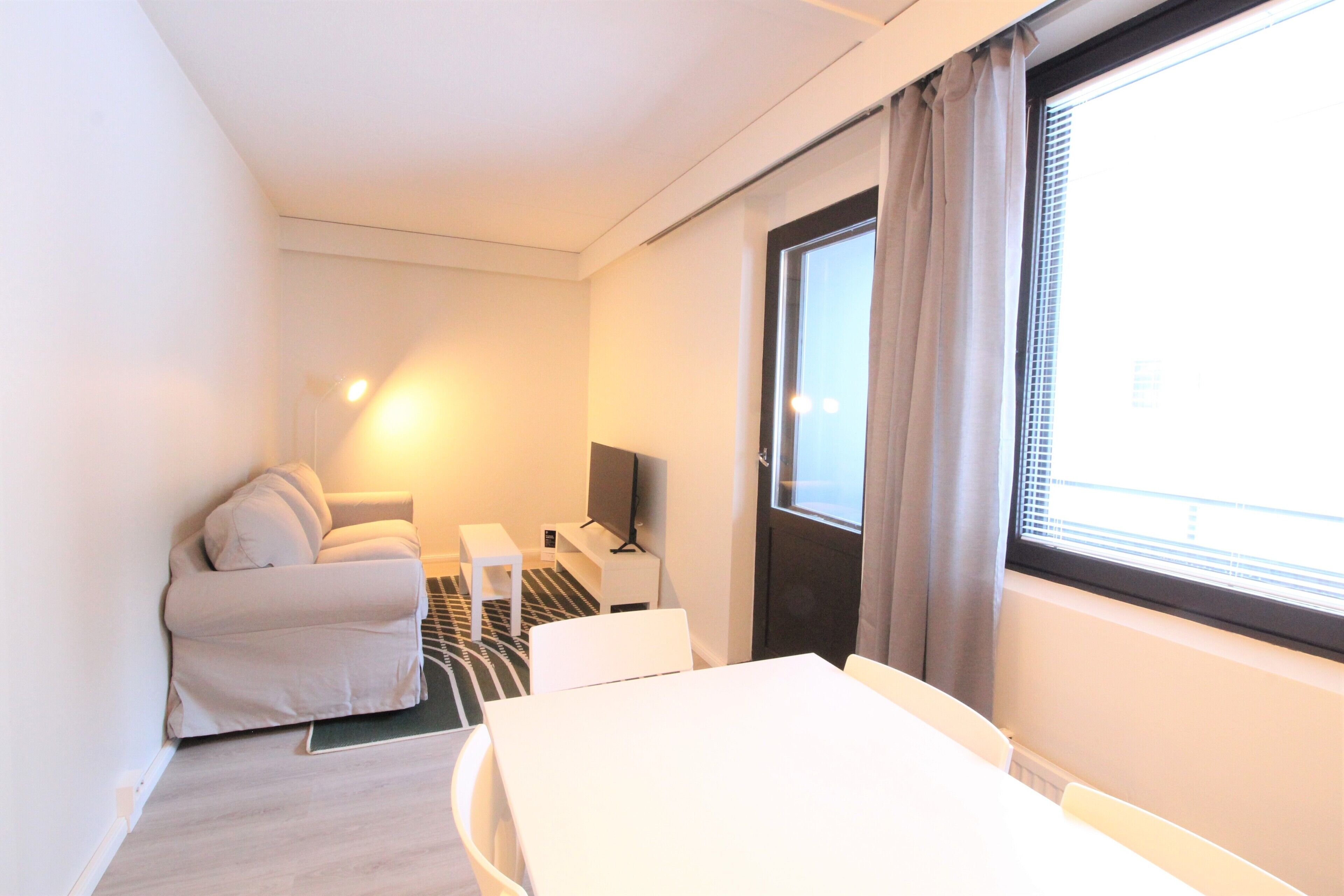 Hotellihuone, jossa on sänky, sohva, televisio ja ikkuna, jossa on verhot.