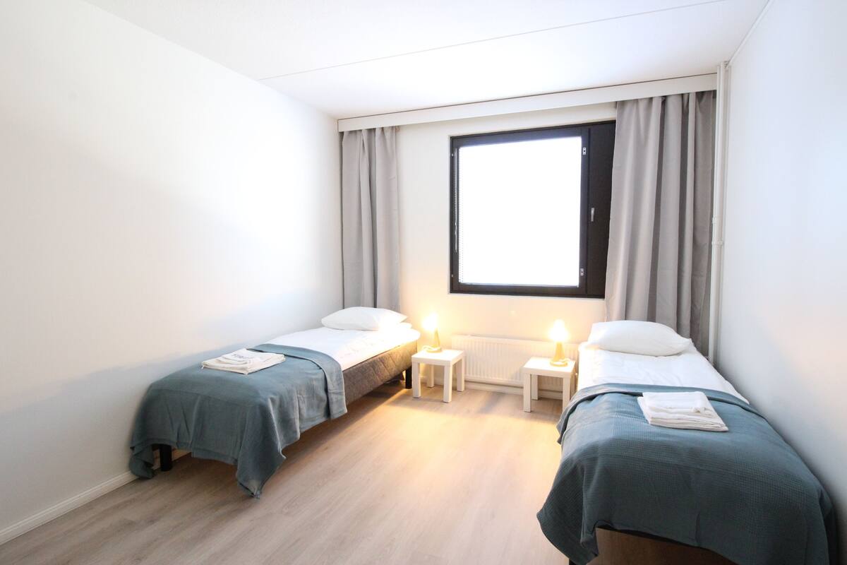 A small, clean room with two single beds, a window with curtains, and a radiator.