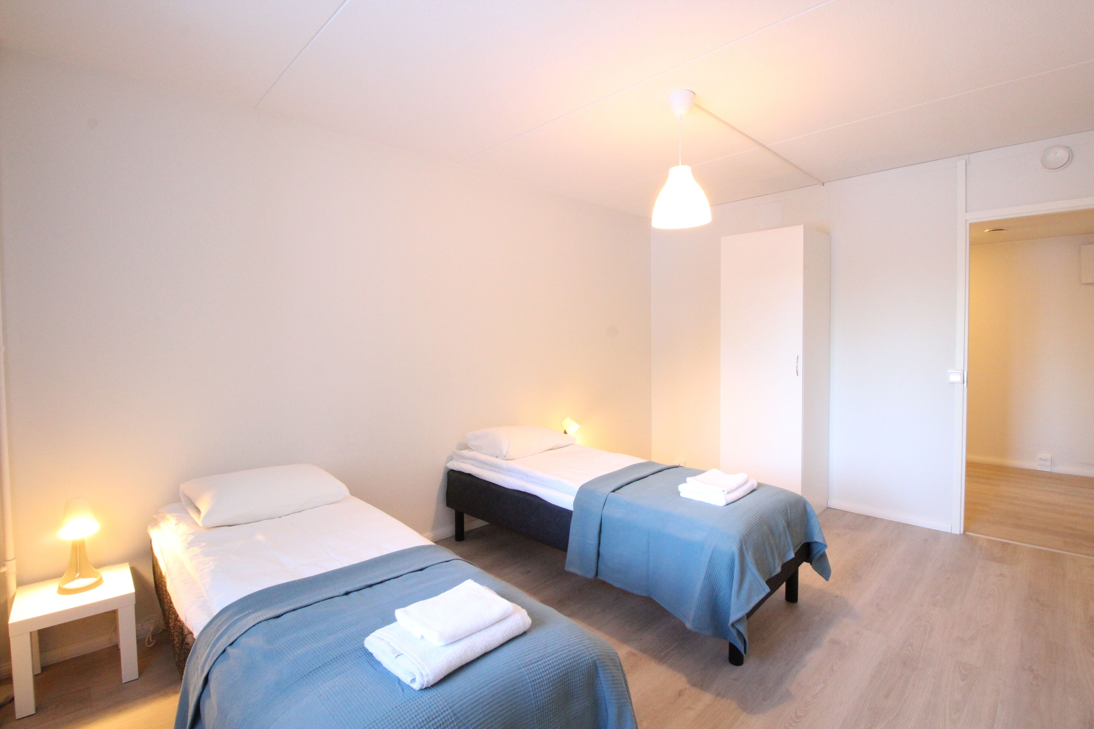 A room with two beds, a nightstand, and a hanging light fixture.