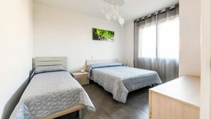 Un dormitorio con dos camas individuales, una mesita de noche, un escritorio y una ventana con cortinas.