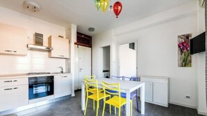 Una cocina moderna con armarios blancos, horno empotrado y una zona de comedor con sillas amarillas.