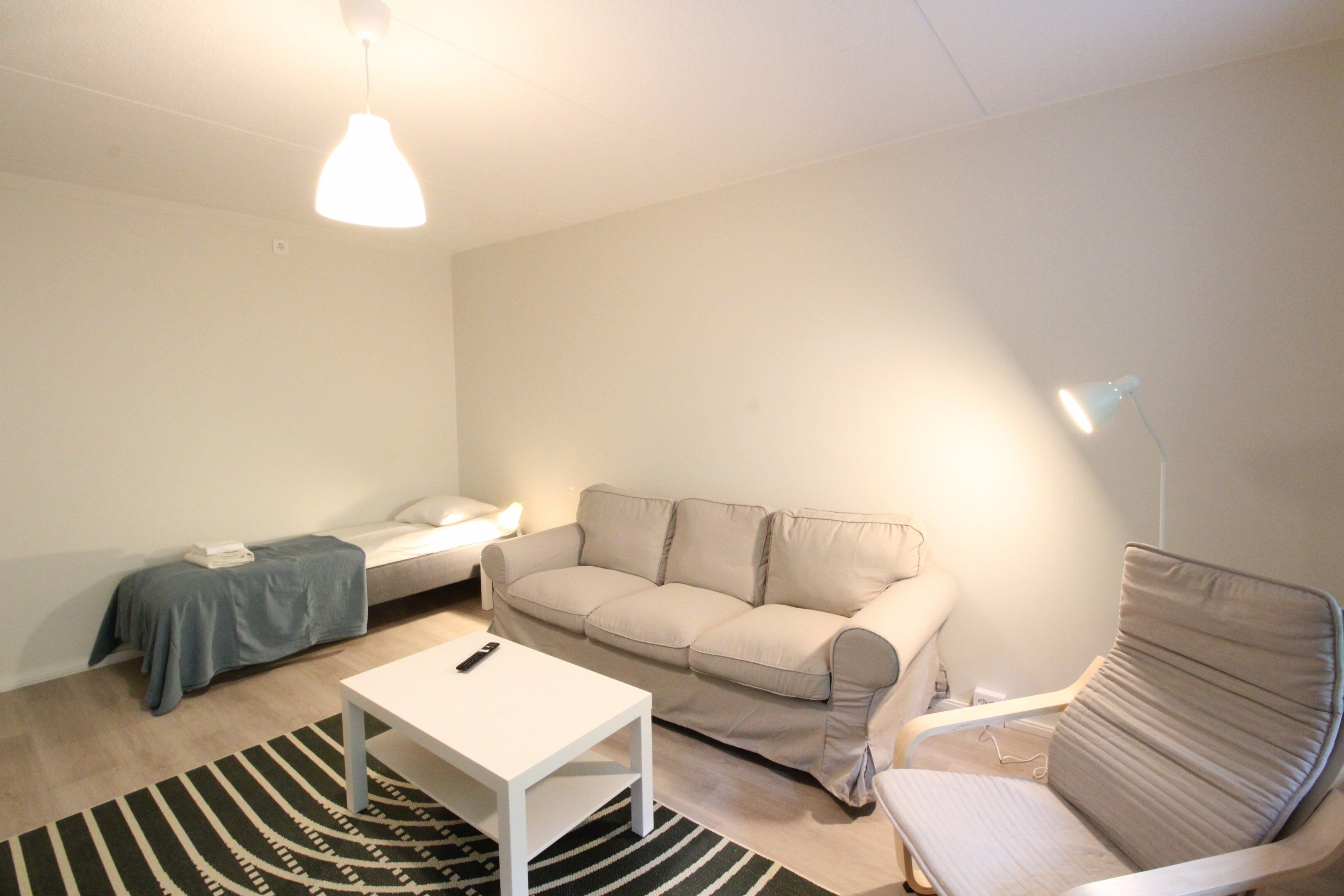 A small, well-lit room with a sofa, a chair, a white table, and a floor lamp.