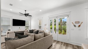 Ein modernes Wohnzimmer mit einem beigefarbenen Ecksofa, einem flachbildfernseher an der Wand und einem Deckenventilator.