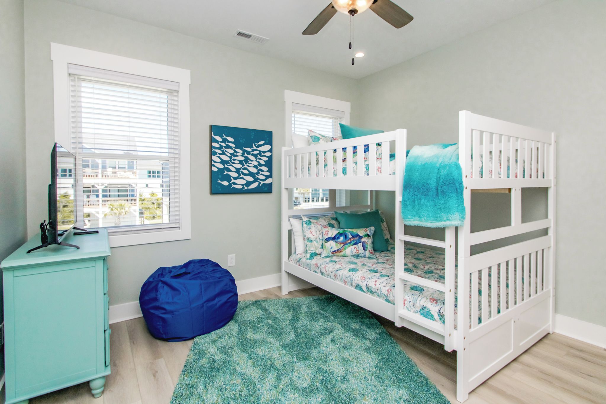 A child's bedroom with bunk beds, a desk, a bean bag, and a view of buildings outside.
