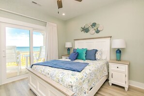 Un dormitorio con cama, mesitas de noche, vista a la playa y ventilador de techo.