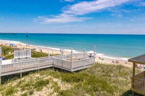 A beach with a wooden boardwalk leading to a sandy beach area, a pier in the distance, and clear blue skies. - Shore N' Tell - Luxury 5BR Home - Cov. Porch, Elevator, Gazebo and More! (Surf City)