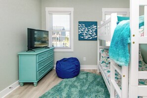 Une chambre d’enfant avec une télévision, une commode, un fauteuil poire, un lit superposé et des œuvres d’art.
