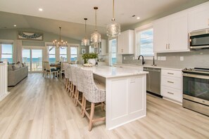 Une cuisine moderne avec des meubles blancs, un îlot central, des tabourets de bar et une vue sur l’extérieur.