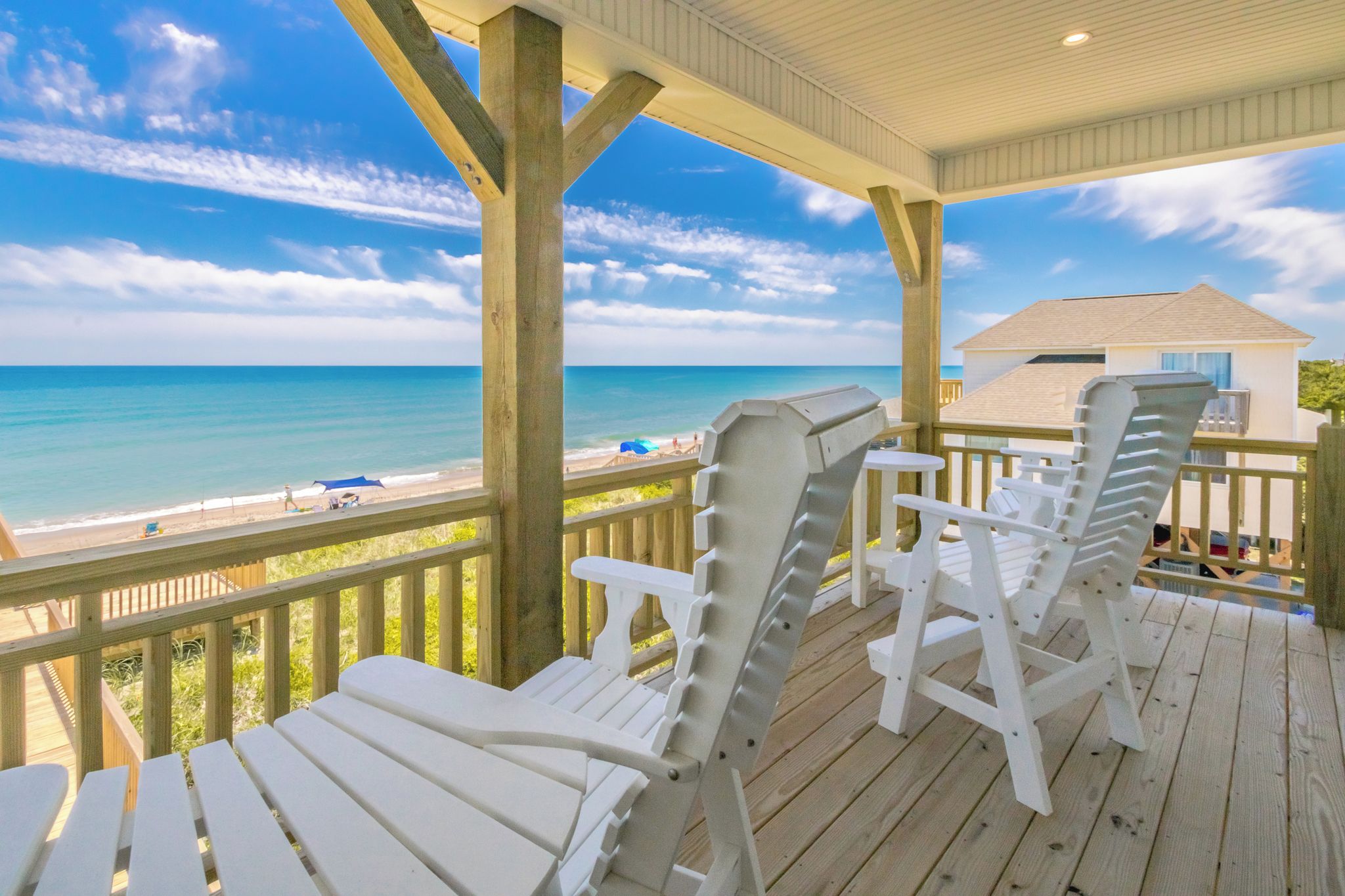 A wooden deck with white lounge chairs overlooking a beach.
