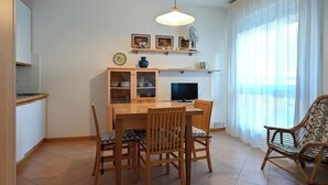 A dining area with a wooden table and chairs, a television, and a shelf with decorative items. - VERA CRUZ 103 (Lido di Jesolo)