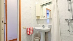 A bathroom with a pedestal sink, a mirror above it, a shower, and a small trash bin. - VERA CRUZ 103 (Lido di Jesolo)