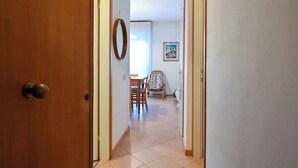 A hallway with a wooden door, a dining area with a table and chairs, and a patterned armchair. - VERA CRUZ 103 (Lido di Jesolo)