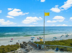 A beach with a wooden boardwalk, beach umbrellas, and a flag. - Cassine Gardens by Panhandle Getaways (Santa Rosa Beach)