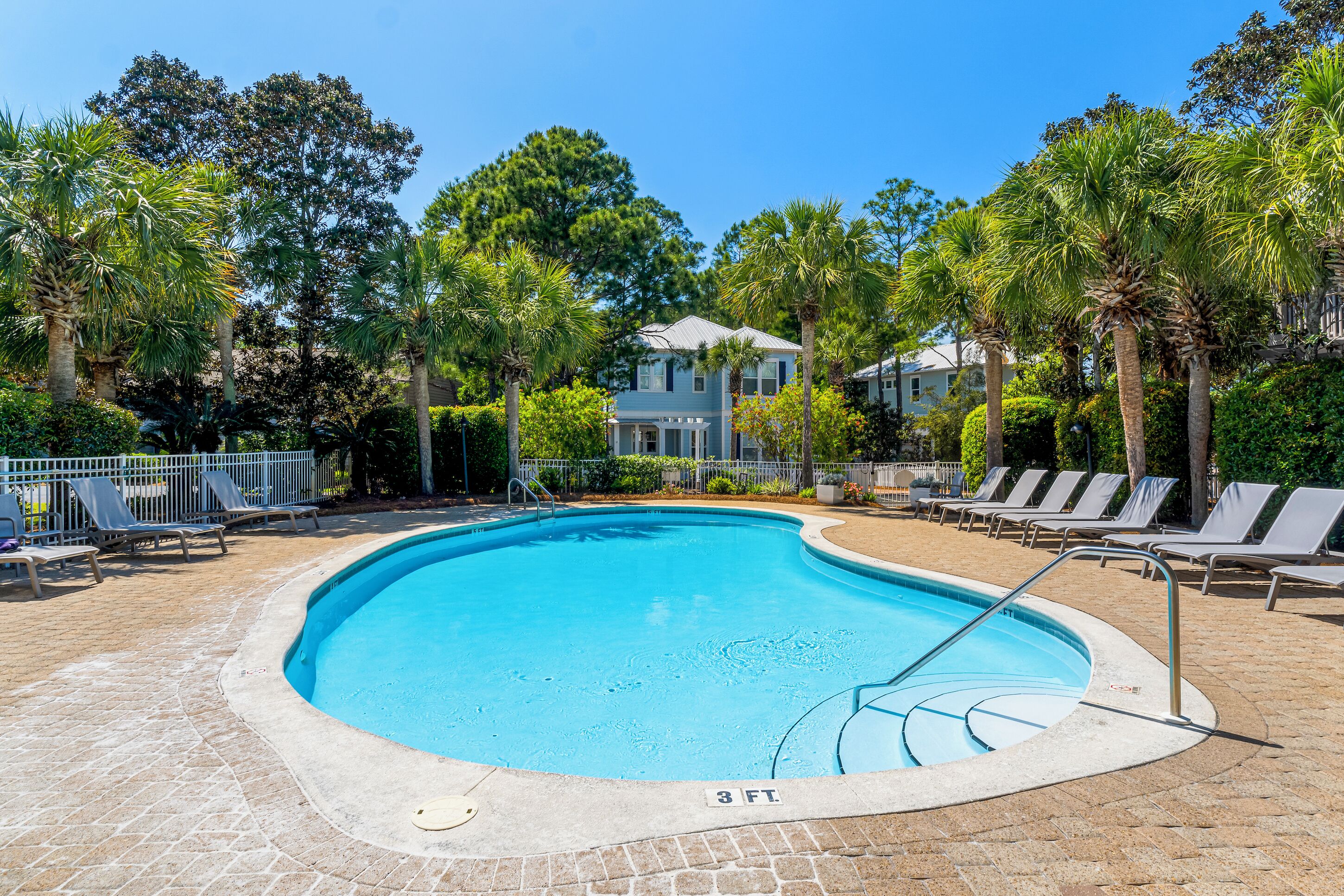 A swimming pool with a 3 ft. depth marker, surrounded by lounge chairs and palm trees.