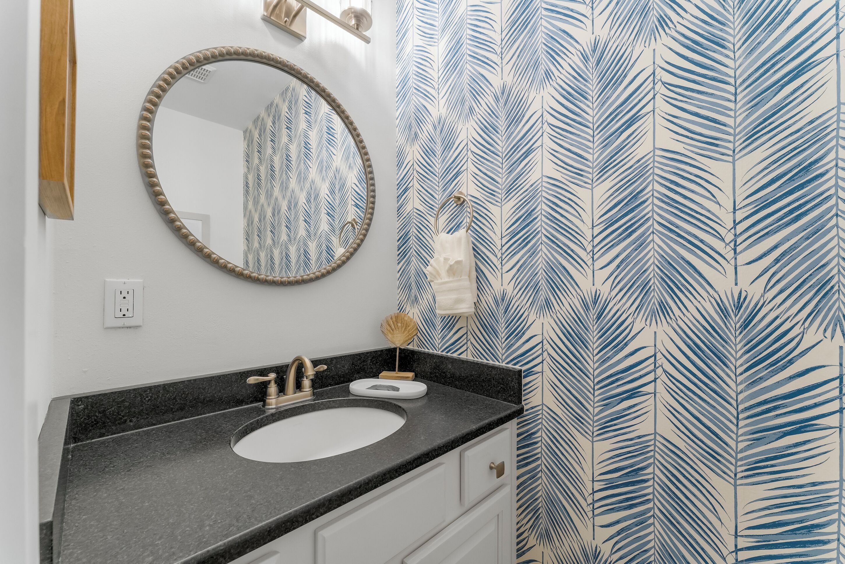A bathroom with a round mirror, a sink, and a towel rack.