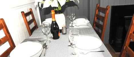 A dining table set with white plates, silverware, and wine glasses, with a bottle of champagne and a vase of white flowers.