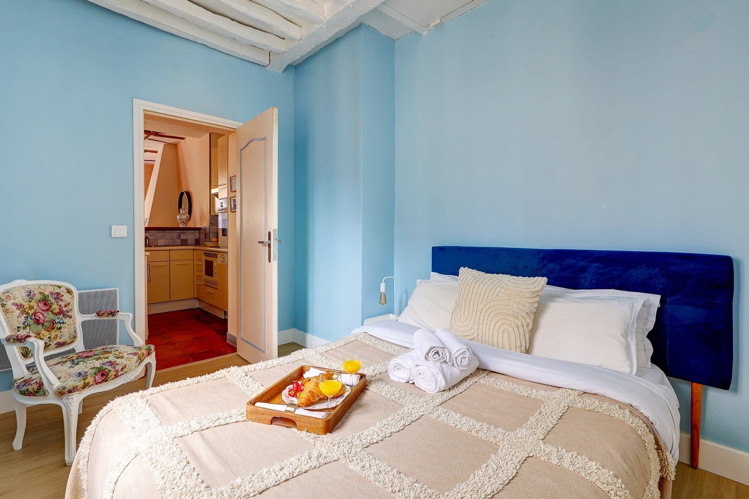 A hotel room with a bed, a breakfast tray, a chair, and a view of the kitchen.