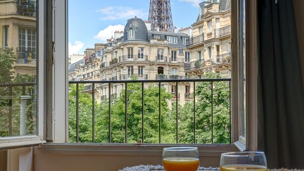 A breakfast tray with croissants and strawberries on a window sill, with a view of the Eiffel Tower and Parisian buildings.