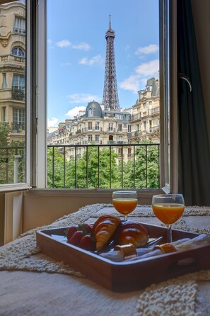 Un plateau de petit-déjeuner avec des croissants et des fraises, posé sur un rebord de fenêtre, d’où l’on peut admirer la Tour Eiffel et les bâtiments parisiens.