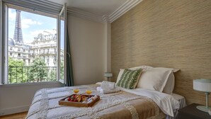 A hotel room with a large bed, a view of the Eiffel Tower, and a breakfast tray on the bed.