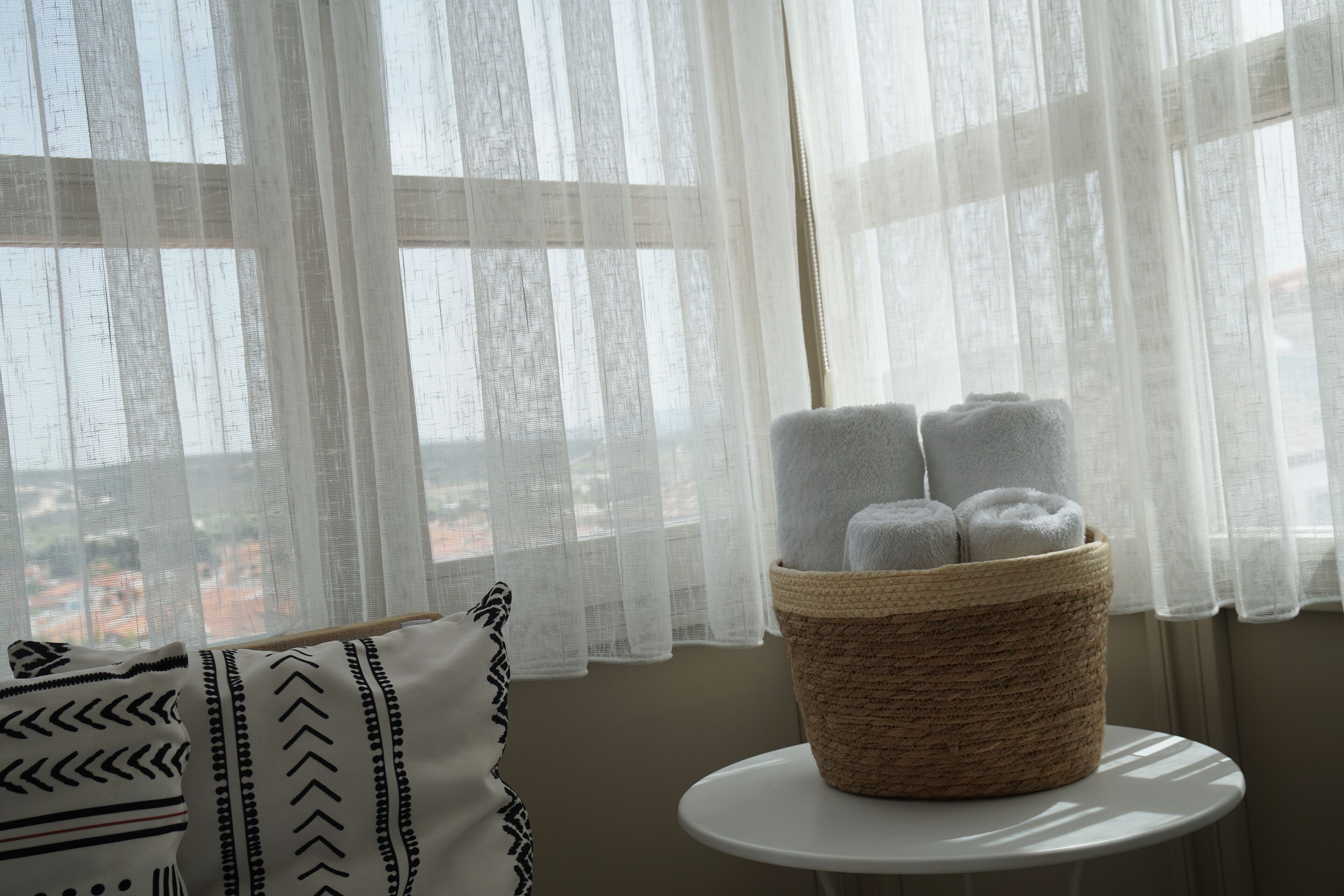 A room with a window, a white table, and a basket of rolled towels.