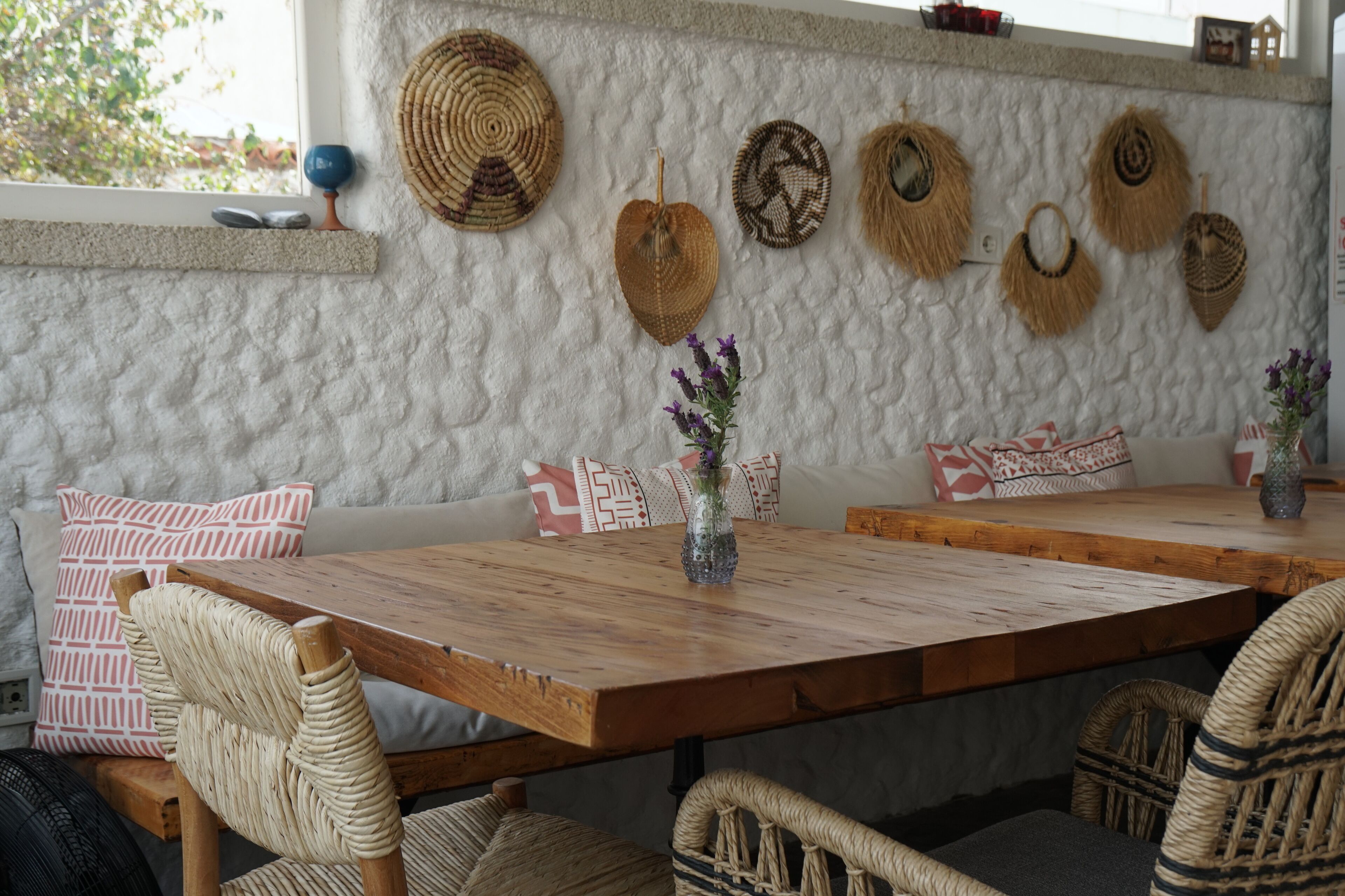 Un comedor acogedor con una mesa de madera y sillas de mimbre, rodeado de cojines estampados y una pared con textura y adornos tejidos.