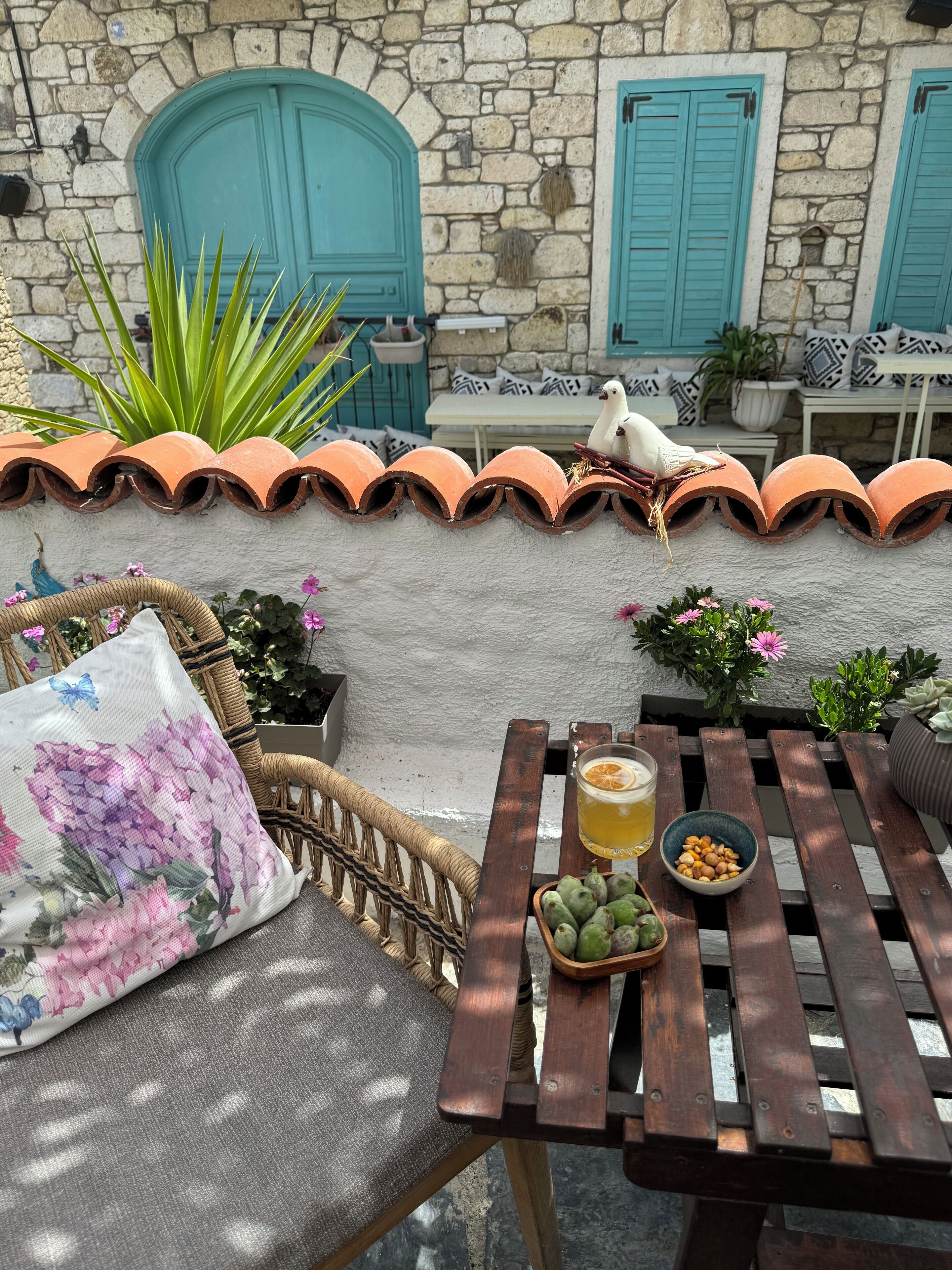 A rustic outdoor seating area with a stone wall, terracotta roof tiles, and a table with a drink and snacks.