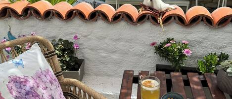 A rustic outdoor seating area with a stone wall, terracotta roof tiles, and a table with a drink and snacks.