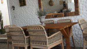 A dining area with a wooden table and wicker chairs, a rustic mirror, and a potted plant. - H&R Alaçatı Hotel (Cesme)