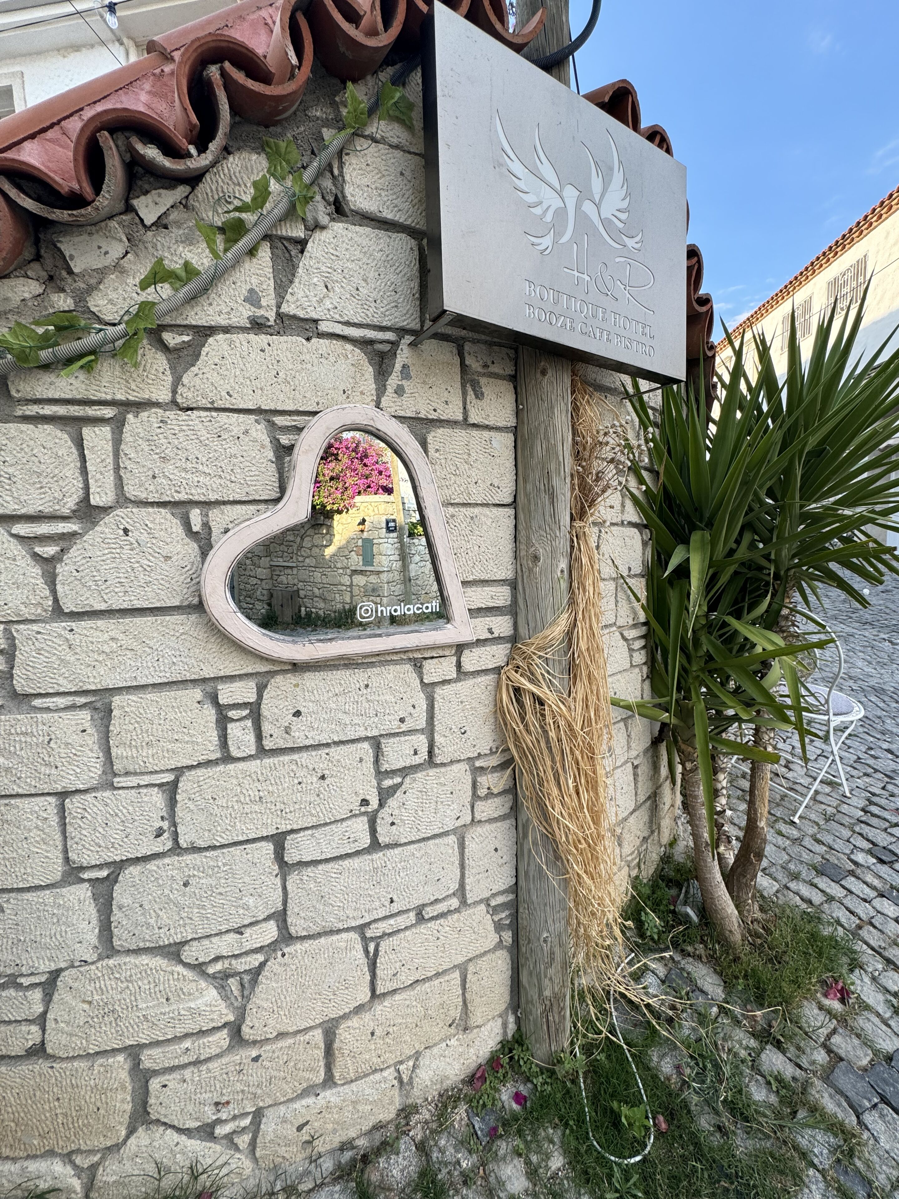 A stone wall with a heart-shaped window, a sign for the Hoh Hotel, and a potted plant.