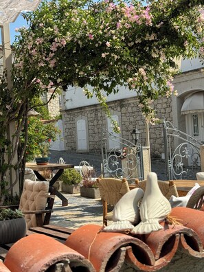 A courtyard with stone buildings, a wrought iron gate, and outdoor seating with cushions and planters. - H&R Alaçatı Hotel (Cesme)