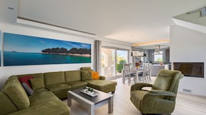 A modern living room with a green sofa, a coffee table, and a dining area with chairs and a table.
