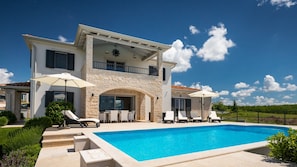 A two-story house with a swimming pool, outdoor seating, and a stone facade.