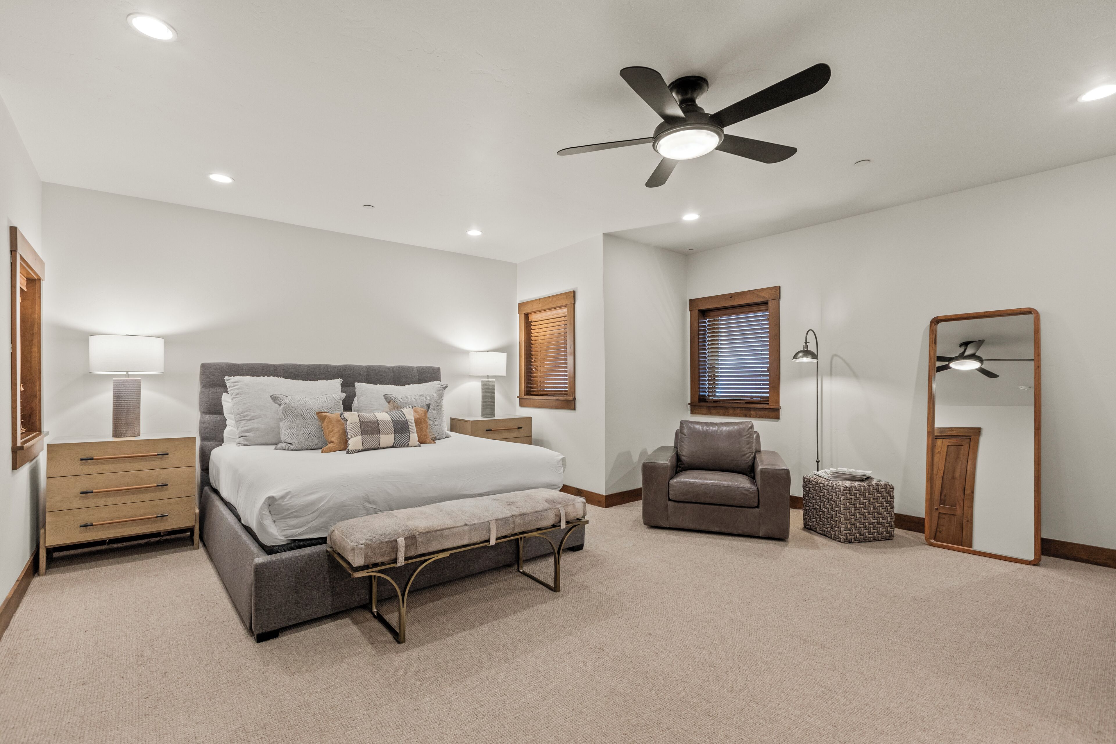 A bedroom with a bed, bedside tables, a chair, a bench, a floor lamp, and a ceiling fan.