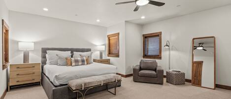 A bedroom with a bed, bedside tables, a chair, a bench, a floor lamp, and a ceiling fan.