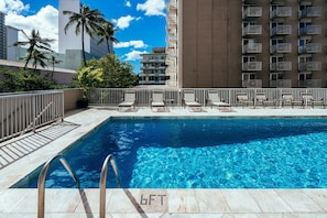 A swimming pool with sun loungers, a metal railing, and a view of high-rise buildings.
