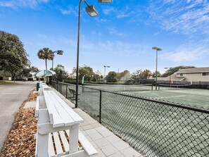 Una cancha de tenis con vallas, bancos y farolas.