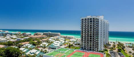 A high-rise hotel with a tennis court and a view of the ocean.