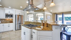 A modern kitchen with white cabinets, stainless steel appliances, granite countertops, and pendant lighting.
