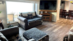 A cozy living room with a sofa, ottoman, and a television. - Paradise Suites in Homer Alaska, an entire house w/a hot tub (Homer)