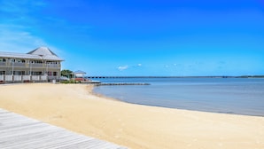 A beach with a wooden boardwalk leading to a building with balconies.