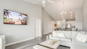 A spacious living room with a large flat-screen TV, a white sectional sofa, and a wooden coffee table.