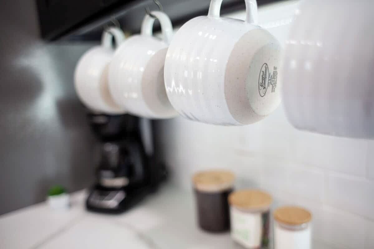 A kitchen with white mugs hanging on a rack, a coffee maker, and jars on the counter.