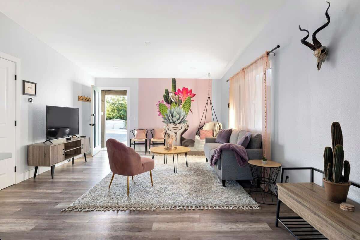 A modern living room with a flat-screen TV, a pink chair, a grey sofa, a round coffee table, and a cactus on a wooden table.