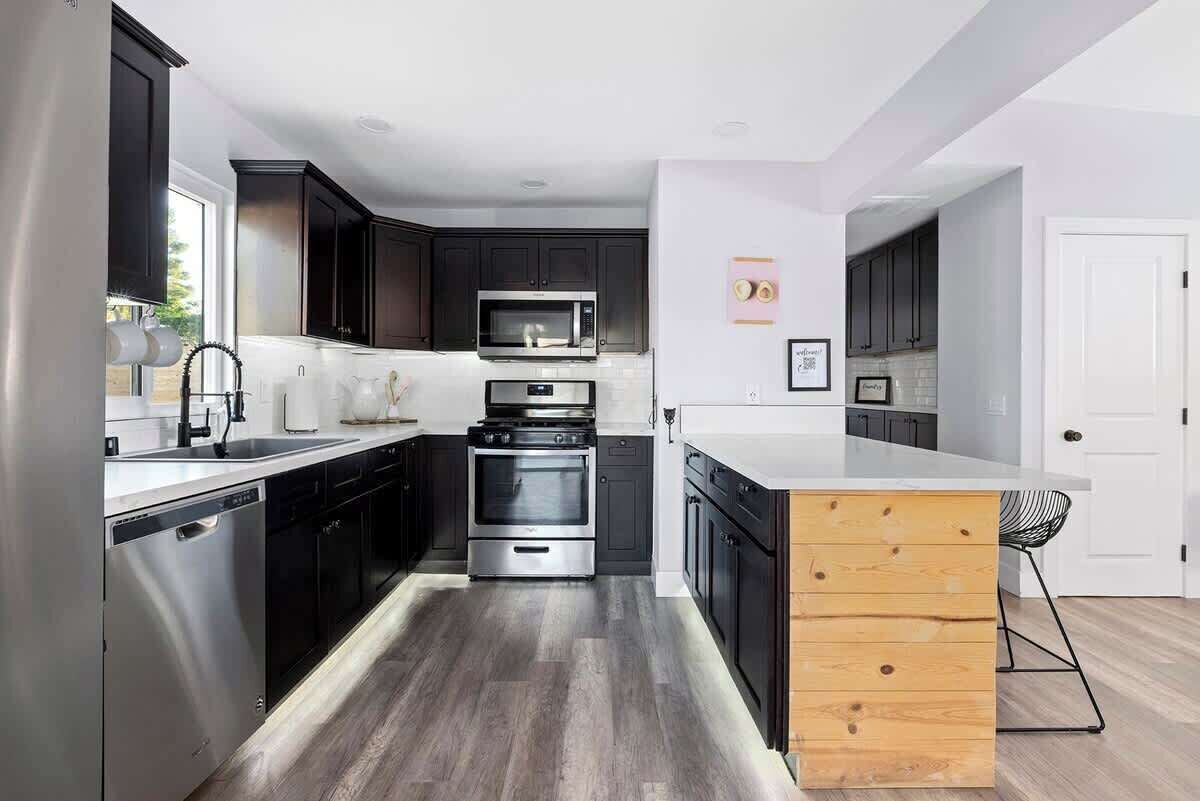 Une cuisine moderne avec des meubles de couleur sombre, des appareils électroménagers en acier inoxydable et un îlot central en bois.